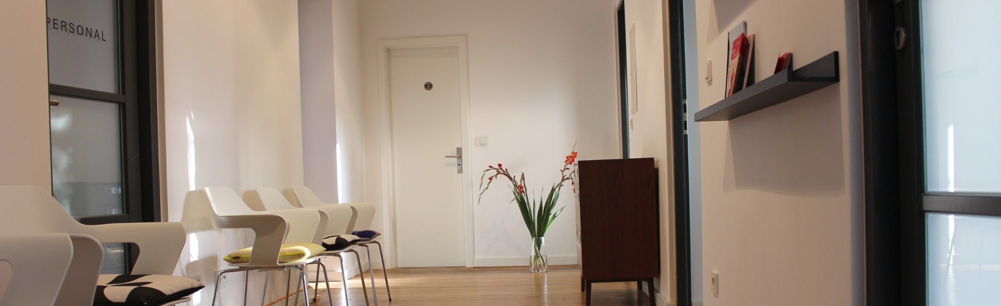 Unser Empfangs- und Wartebereich Moderner, heller Empfangs- und Wartebereich von psyvia, mit weißen Designer-Stühlen, Holzboden und Deko-Pflanze